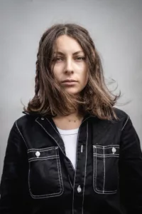 Portrait studio sur fond gris clair d'une surfeuse avec de long cheveux bruns et tresses