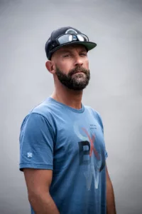 Portrait studio sur fond gris clair d'un moniteur de surf en casquette et portant une barbe