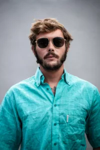 Portrait studio sur fond gris clair d'un surfeur en en chemise turquoise et lunettes de soleil