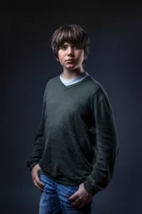 Portrait studio d'un enfant en pull et jeans sur fond gris foncé